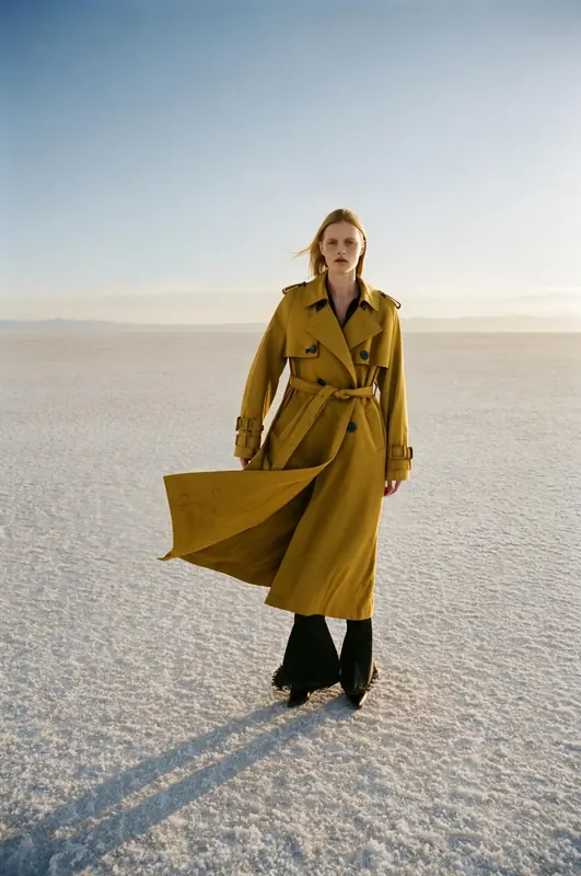 FLUX 3 Klein example: A model in a mustard trench coat on a white salt flat, the coat blowing sideways.