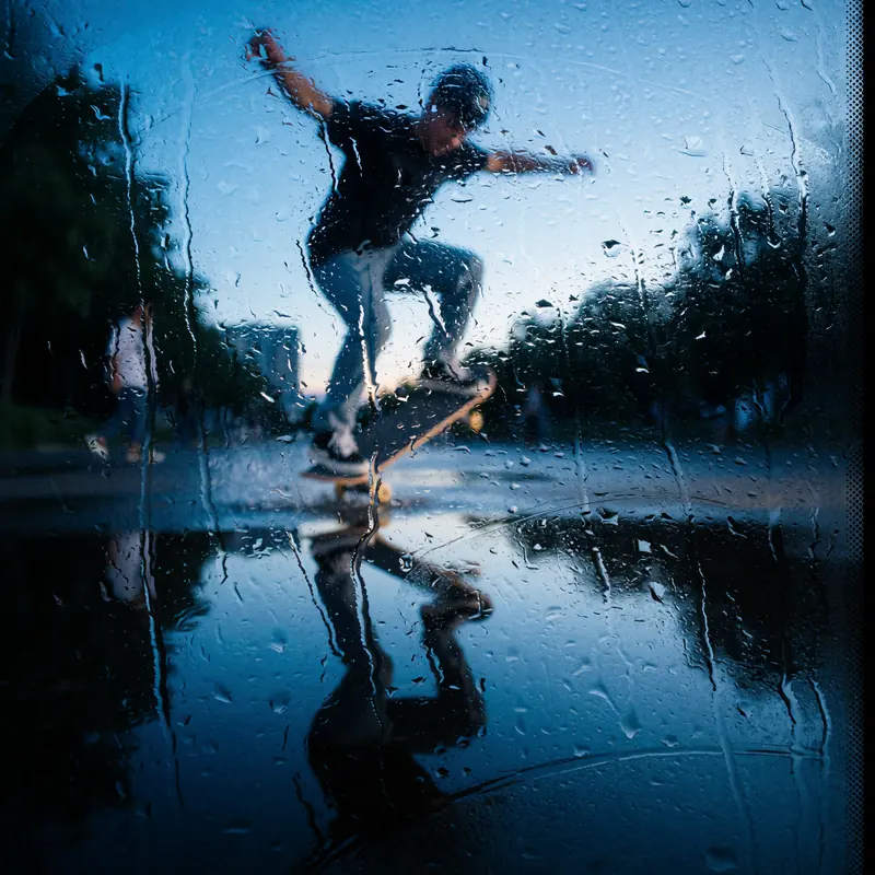 Krea 2 example: A skateboarder doing a kickflip at blue hour, a puddle reflects the skateboarder. rainy window style