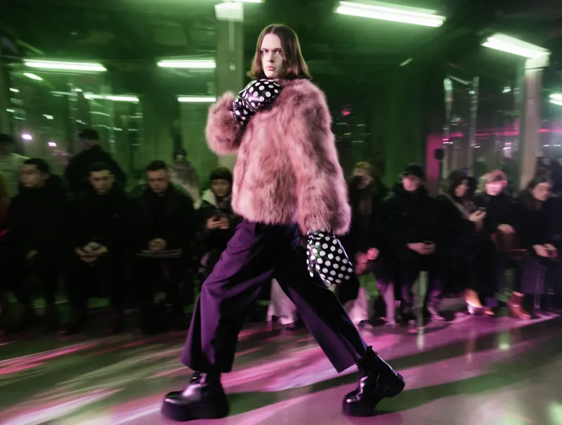 Krea 2 example: Over-the-shoulder tracking shot of a model walking with exaggerated runway gait — torso twisted unnaturally to look dire